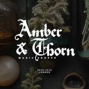 May include: A dark image with the text "Amber & Thorn MAGIC SHOPPE ESTD 2018 LONDON" in a gothic font. The image includes jars with plant life and a light-coloured sphere, suggesting a mystical or apothecary theme.