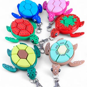May include: A collection of colorful turtle-shaped keychains. Each keychain features a different color scheme, including blue, pink, red, green, yellow, and teal. The turtles have segmented shells and are attached to silver-colored clasps.