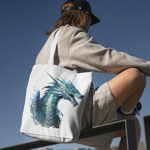 May include: A white tote bag with a blue and green dragon design. The dragon is facing the right side of the bag and has a fierce expression. The bag has two long straps.