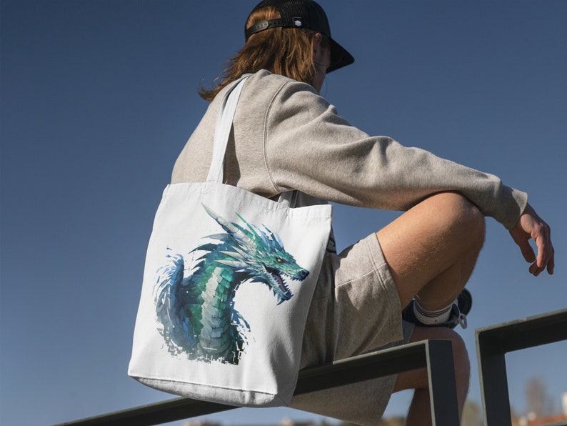 May include: A white tote bag with a blue and green dragon design. The dragon is facing the right side of the bag and has a fierce expression. The bag has two long straps.