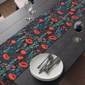 May include: A dark blue table runner with a floral pattern featuring red poppies and green leaves. The runner is laid out on a dark wood table with two chairs and a bowl of fruit.