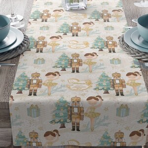 May include: A white table runner with a repeating pattern of nutcracker soldiers, ballerinas, Christmas trees, and presents. The pattern is in shades of brown, green, and gold.