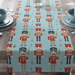 May include: A blue table runner with a repeating pattern of nutcracker soldiers and Christmas trees. The nutcracker soldiers are wearing red and blue uniforms and holding golden swords.