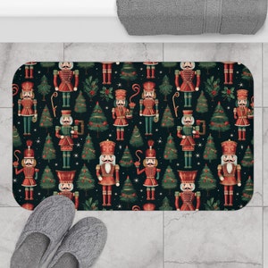 May include: A black bath mat with a repeating pattern of nutcracker soldiers and Christmas trees. The nutcracker soldiers are wearing red and gold uniforms and holding a staff. The Christmas trees are green and decorated with red berries. The background is a dark blue color with white stars.
