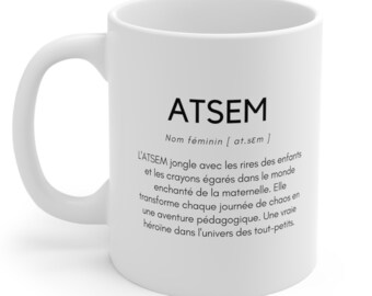 May include: White ceramic mug with a black graphic design that reads "ATSEM Nom féminin [at.sɛm] L'ATSEM jongle avec les rires des enfants et les crayons égarés dans le monde enchanté de la maternelle. Elle transforme chaque journée de chaos en une aventure pédagogique. Une vraie héroïne dans l'univers des tout-petits."