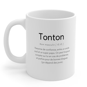 Könnte beinhalten: Weiße Keramiktasse mit einem schwarzen Design, das das Wort "Tonton" als französisches maskulines Nomen definiert, das eine vertraute Person bedeutet, wie ein cooler Onkel oder ein super Papa. Der Text lautet "Tonton, Nom masculin [15.15] Personne de confiance, entre un oncle cool et un super papa. On peut toujours compter sur lui en cas de problèmes, et parfois pour de bonnes blagues (ça dépend des jours)."