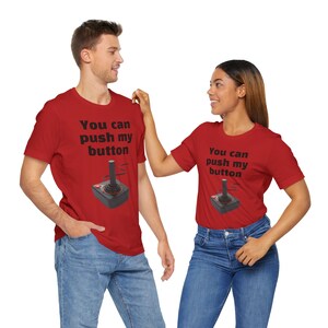 Puede incluir: Dos camisetas rojas con un gráfico de joystick negro y el texto "You can push my button".