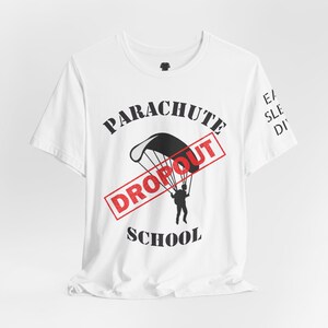 May include: White t-shirt with a black and red graphic. The design features a parachute with a person, the words "PARACHUTE SCHOOL" and a red "DROPOUT" stamp. The sleeve has the words "EAT SLEEP DIVE".