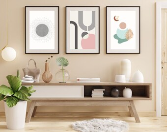 Peut inclure: Trois impressions d'art abstrait encadrées avec des formes géométriques et des couleurs. Les impressions sont accrochées à un mur beige clair au-dessus d'une étagère en bois avec un tiroir blanc et deux étagères ouvertes. L'étagère est décorée de plantes, de livres et d'objets décoratifs.