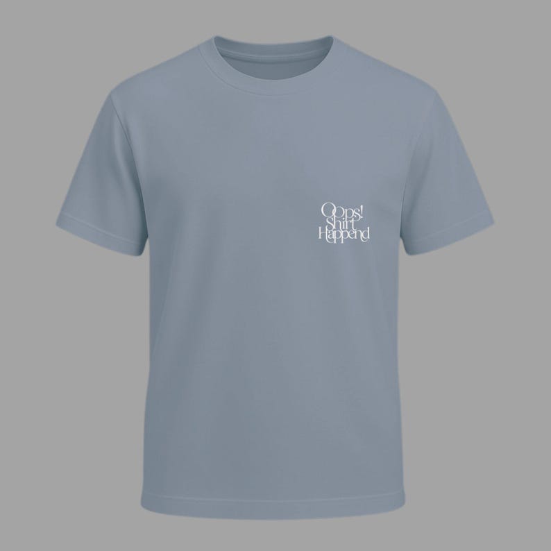 May include: A light blue t-shirt with short sleeves. The shirt features the text "Oops! Shirt Happened" in white script on the upper left chest area. The shirt is made of a soft material and has a crew neck.