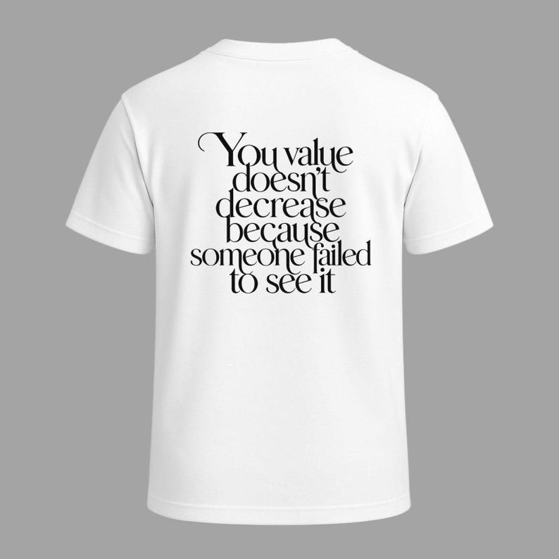 May include: White t-shirt with the quote "You value doesn't decrease because someone failed to see it" printed in black. The shirt has short sleeves and a crew neck, suitable for casual wear.
