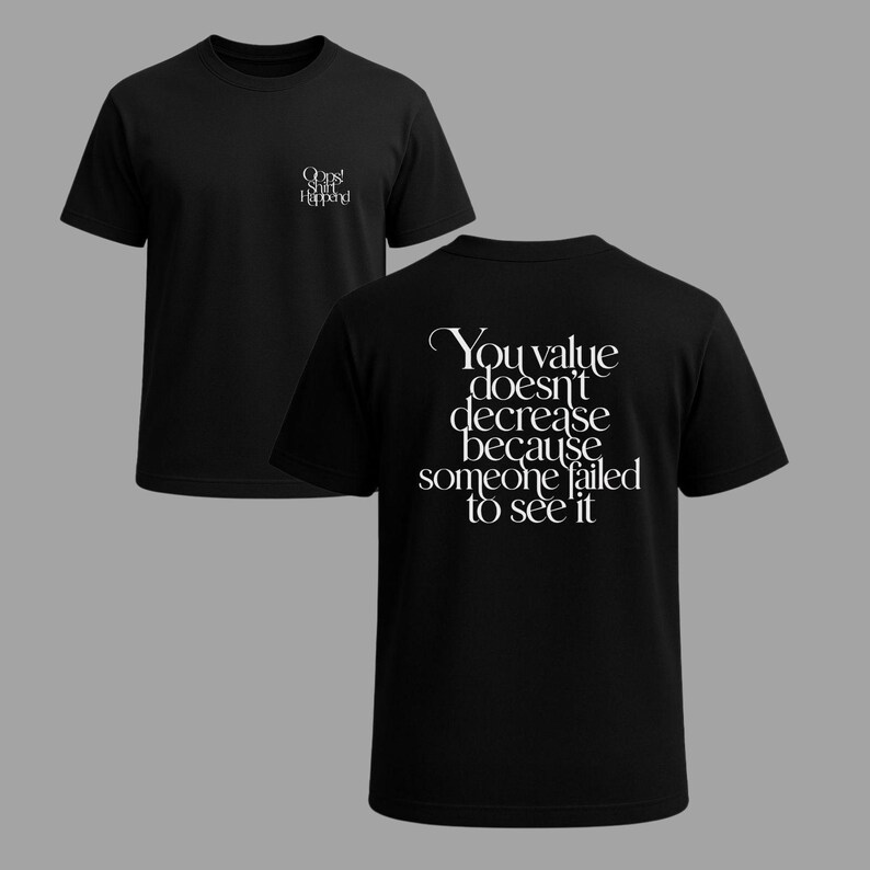May include: Black t-shirts with white text. One shirt displays "Oops! Shit Happened" on the front. The other shirt has the text "You value doesn't decrease because someone failed to see it" on the back. Both shirts have a crew neck.