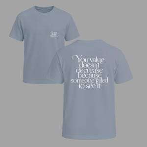 May include: Two light blue t-shirts. One shirt has the text "Ghost Ships Happening" on the front. The other shirt has the text "You value doesn't decrease because someone failed to see it" on the back.