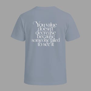 Può includere: T-shirt azzurra con la scritta bianca: "You value doesn't decrease because someone failed to see it". La maglietta ha maniche corte e girocollo, ideale per l'uso quotidiano.