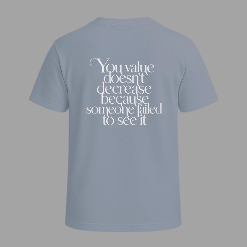 May include: A light blue t-shirt with the text "You value doesn't decrease because someone failed to see it" in white script. The shirt has short sleeves and a crew neck, suitable for casual wear.