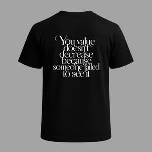 May include: Black t-shirt with the white text "You value doesn't decrease because someone failed to see it." The shirt has short sleeves and a crew neck. The text is in a decorative font.