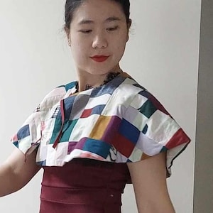 May include: A woman wearing a maroon skirt with a colourful patterned top. She is standing on a staircase with a wooden handrail.