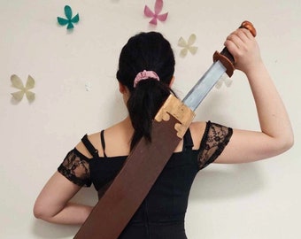 May include: A person wearing a black dress with a brown leather scabbard strapped across their back. A silver sword with a brown handle is held in their right hand.