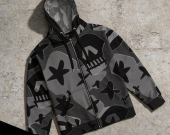 May include: A zip-up hoodie in shades of gray and black featuring a repeating pattern of stylized skulls and star shapes. The garment includes a drawstring hood, a full-length front zipper, ribbed cuffs, and a hem. Text at the bottom reads 4 DESIGN OPTIONS.