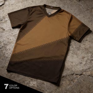 Könnte beinhalten: Ein kurzärmeliges V-Ausschnitt-Shirt mit einem diagonalen Farbblock-Design in Dunkelbraun- und Beigetönen. Das Kleidungsstück weist ein dezentes strukturiertes Muster entlang der diagonalen Linien auf und zeigt den Text 7 COLOR OPTIONS.