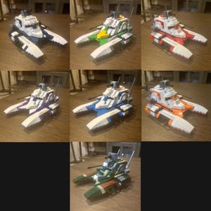 May include: A selection of toy tanks in different colours, including white, blue, green, red, purple, and orange. Each tank has a central turret, side cannons, and a catamaran-style hull. The tanks are made of plastic and look like they are built from construction bricks.