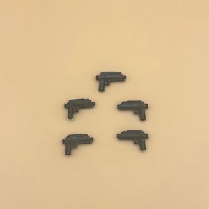 May include: Five black plastic toy guns on a light brown background.
