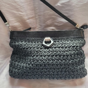 May include: A black woven crossbody bag with a black leather flap and a silver metal clasp. The bag has a long black strap.