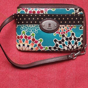 Cartera Fossil de mano con estampado de mandala, lona revestida, cierre de cremallera y correa de cuero marrón.