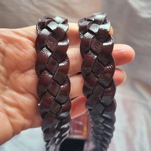 May include: Two dark brown leather straps with a braided design. The straps are woven together and have a glossy finish.