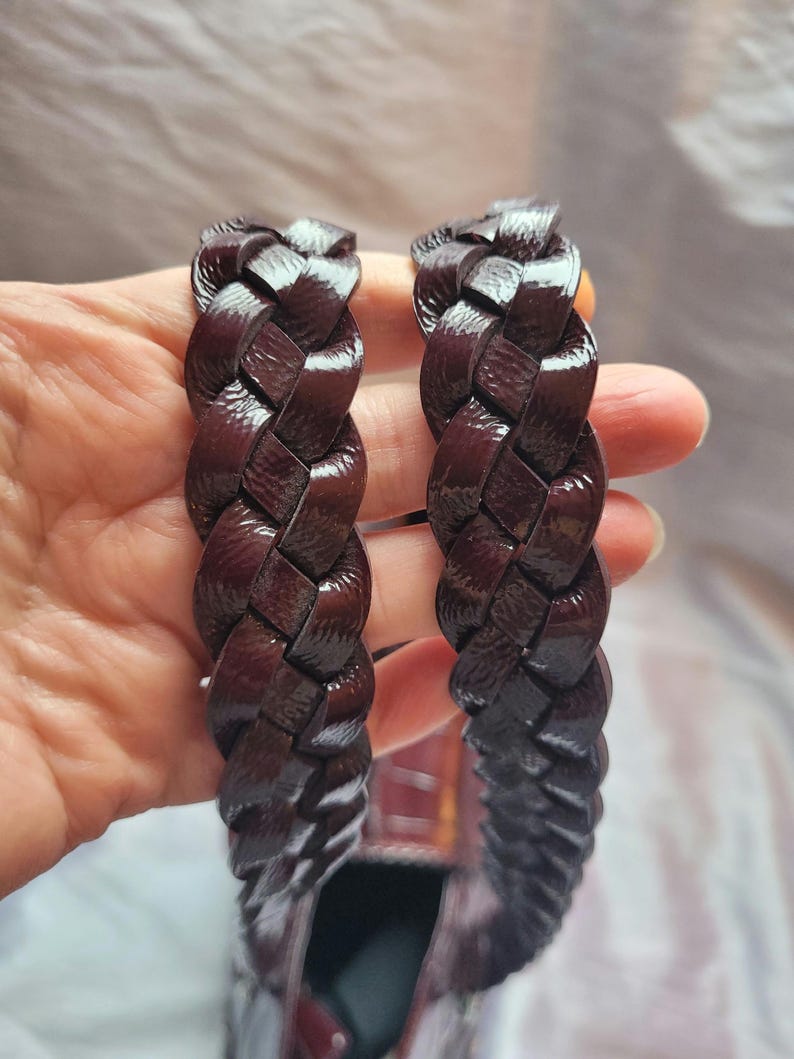 May include: Two dark brown leather straps with a braided design. The straps are woven together and have a glossy finish.
