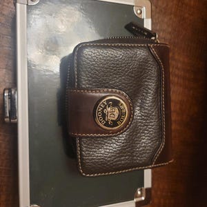 Cartera vintage unisex de Dooney and Bourke de piel auténtica en color negro y marrón con combinación de piel de vaca y cuero granulado y cierre de cremallera en la parte superior con medallón