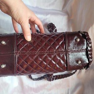 May include: A burgundy quilted leather handbag with a braided strap and silver hardware.