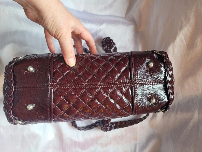 May include: A burgundy quilted leather handbag with a braided strap and silver hardware.