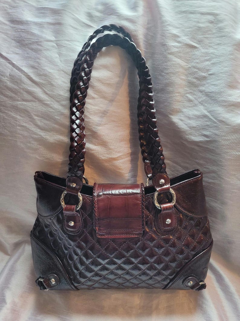 May include: A brown leather handbag with a quilted design and a braided strap. The handbag has a flap closure with a decorative buckle.