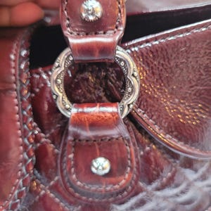 May include: Close-up of a brown leather handbag with a silver metal clasp and decorative stitching. The bag has a quilted texture.