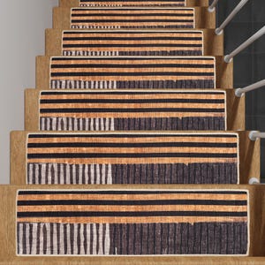 Puede incluir: Un conjunto de peldaños antideslizantes para escaleras con un patrón de rayas blancas y negras y un borde marrón. Los peldaños están hechos de un material texturizado y están diseñados para ayudar a prevenir resbalones y caídas en las escaleras.