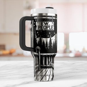 May include: A black and silver stainless steel travel mug with a black handle. The mug has a graphic of a cabin in the woods with a sign that reads "Ew, People".
