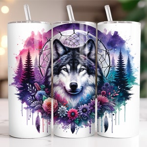 May include: A white tumbler with a watercolor design of a wolf, flowers, and a dreamcatcher. The wolf is gray and white with blue eyes. The flowers are pink, purple, and blue. The dreamcatcher is black and white.
