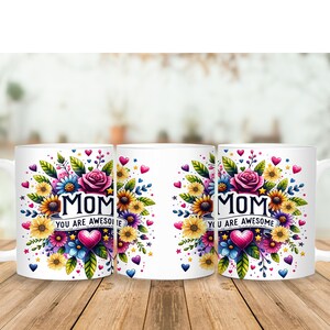 Pu&ograve; includere: Tre tazze in ceramica bianca con un design floreale e il testo "Mom You Are Awesome" in lettere colorate. Le tazze hanno un manico bianco e sono disposte in fila su una superficie di legno.