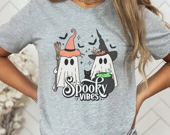 May include: A gray t-shirt with a graphic of two ghosts wearing witch hats, one holding a broom and the other a cauldron. The text "Spooky Vibes" is below the ghosts.