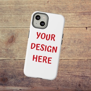 May include: White phone case with the text "YOUR DESIGN HERE" in red. The case has a black border and a camera cutout. The background is a wooden surface.