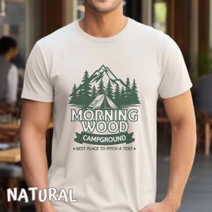 Puede incluir: Una camiseta blanca con un dise&ntilde;o gr&aacute;fico verde de una cordillera, &aacute;rboles y una tienda de campa&ntilde;a. El texto "Morning Wood Campground" est&aacute; impreso en verde debajo del gr&aacute;fico. El texto "Best Place to Pitch a Tent" est&aacute; impreso en verde m&aacute;s peque&ntilde;o debajo del nombre del camping.