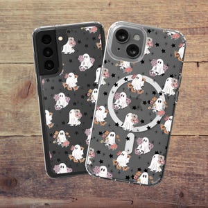 May include: Two clear phone cases with a black background and a repeating pattern of white ghosts, pink and orange flowers, and black stars. The case on the right has a black ring holder.