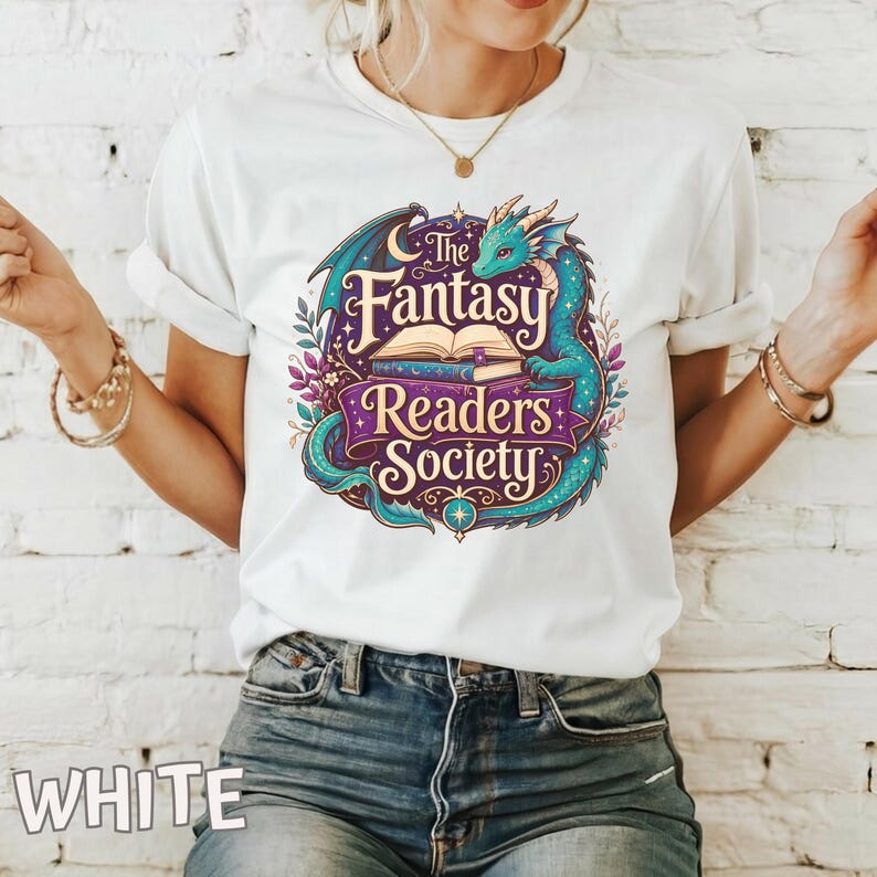 May include: A white short-sleeve t-shirt featuring a colorful graphic of a teal dragon curled around an open book. The text reads The Fantasy Readers Society in stylized lettering. The design includes floral elements, stars, and a crescent moon.