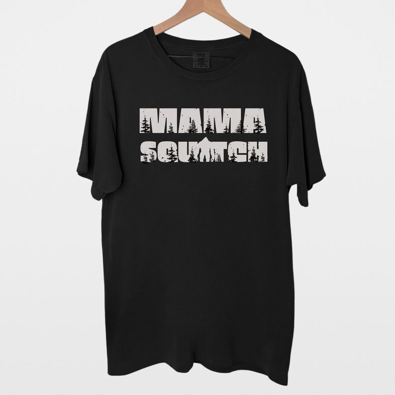 May include: Black t-shirt with a white graphic print that says "Mama Squatch" with a mountain and trees in the background.