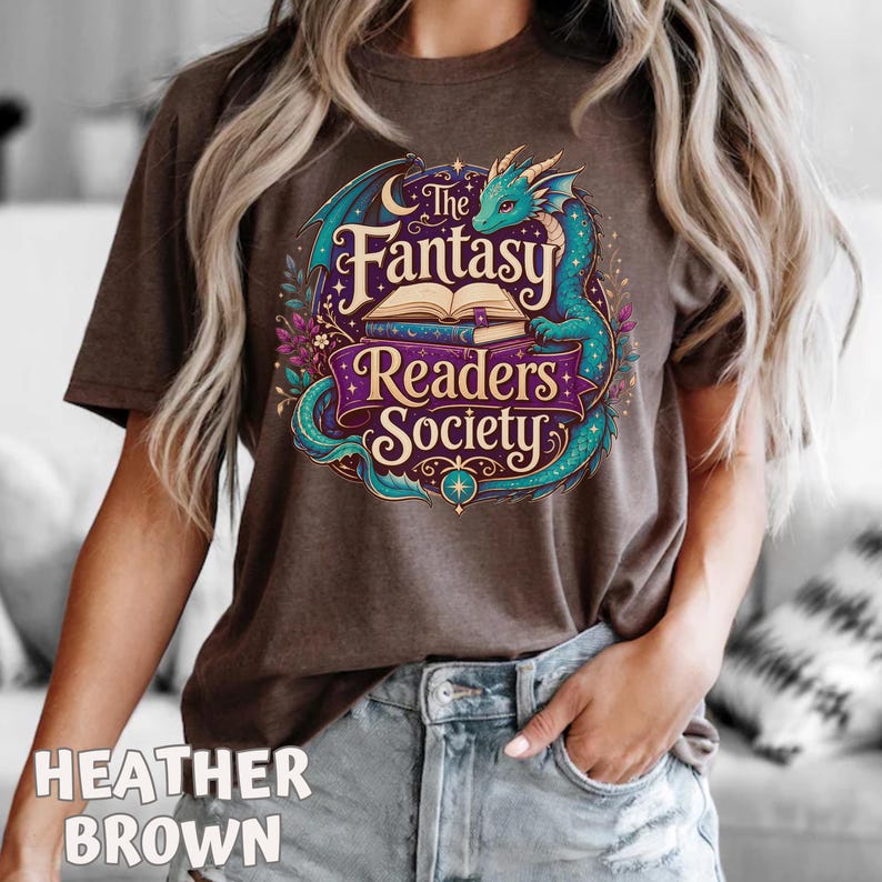 May include: A heather brown t-shirt featuring a graphic print of a teal dragon coiled around an open book. The text reads The Fantasy Readers Society in stylized lettering, surrounded by purple banners, floral accents, and small stars.