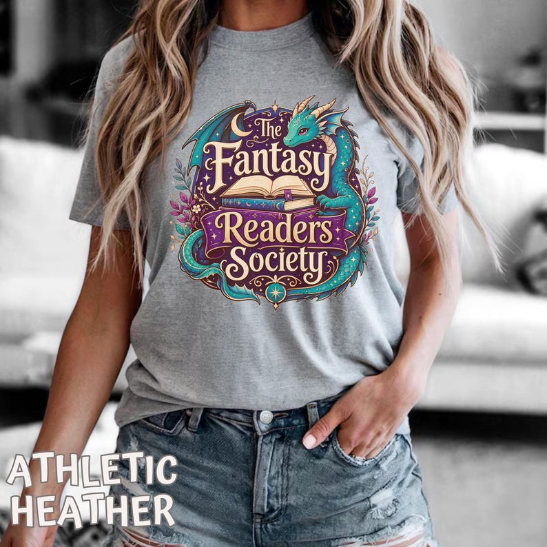 May include: A heather gray short-sleeve t-shirt featuring a graphic print of a teal dragon coiled around an open book. The text reads The Fantasy Readers Society in cream and purple lettering, surrounded by decorative floral elements and stars.