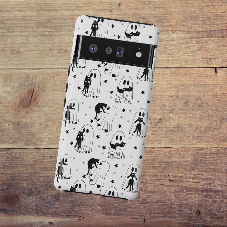 May include: White phone case with a black and white pattern of ghosts and cats. The case has a black camera lens cutout.
