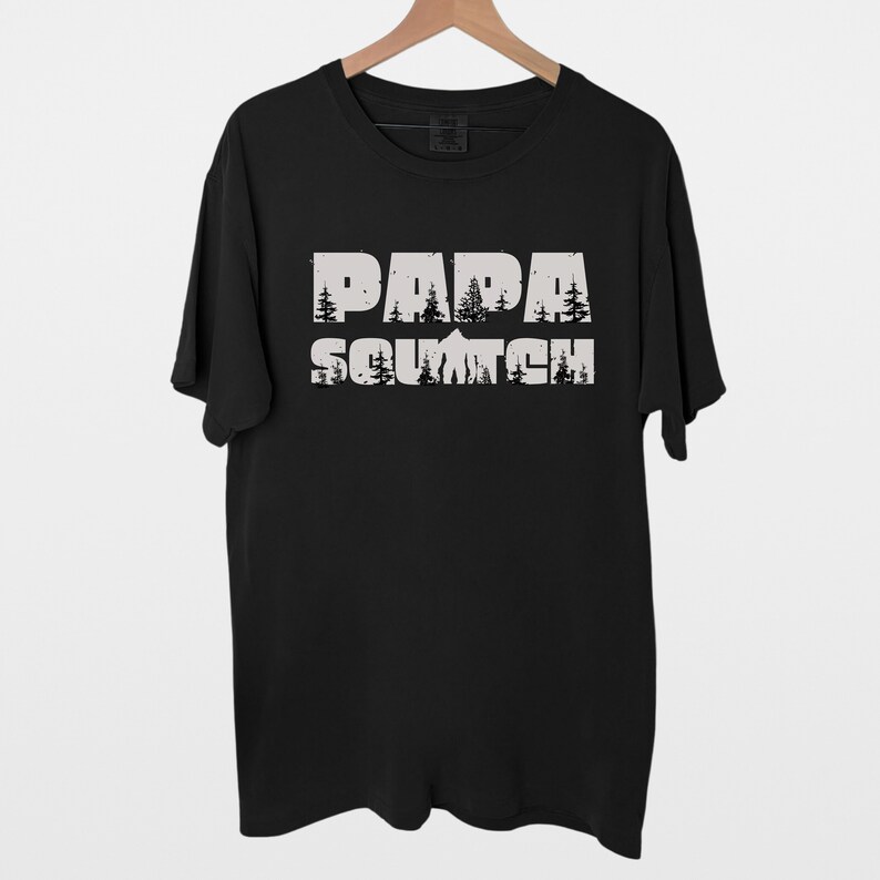 May include: Black t-shirt with a white graphic print that says "Papa Squatch" with a silhouette of a mountain and trees behind the text.