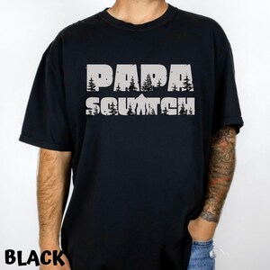 May include: Black t-shirt with a white graphic print that says "Papa Squatch" with a stylized image of a Bigfoot and trees.